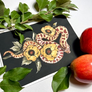 Puede incluir: Una pintura de acuarela de una serpiente envuelta alrededor de tres flores amarillas con marcas rojas y marrones sobre un fondo negro.
