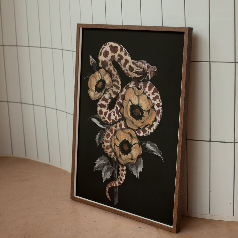 Puede incluir: Una impresi&oacute;n enmarcada de una serpiente envuelta alrededor de un ramo de flores. La serpiente es marr&oacute;n y negra con un patr&oacute;n moteado. Las flores son de color marr&oacute;n claro con un centro amarillo. El fondo es negro.