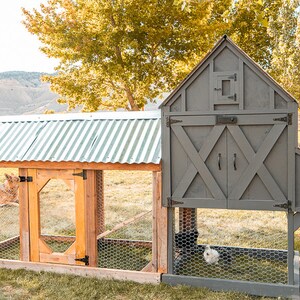 May include: A gray and natural wood chicken coop with a corrugated metal roof. The coop has a fenced run and a separate enclosed house with a door. A dog is resting inside the run, and a chicken is inside the house.