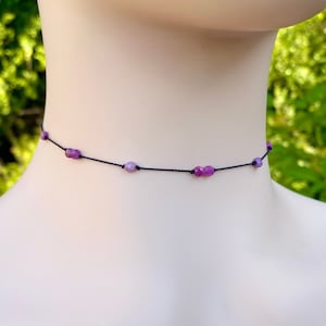 May include: A delicate choker necklace with a black cord and small purple beads.