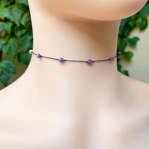 May include: A delicate choker necklace with a black cord and small purple amethyst beads.