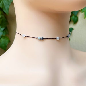 May include: A delicate choker necklace with a black cord and small white and gray gemstone beads.