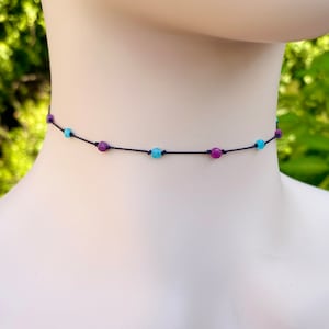 May include: A delicate choker necklace with alternating turquoise and purple beads on a black cord.