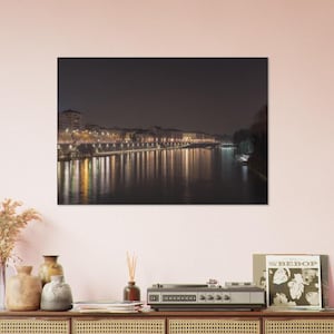 May include: A nighttime cityscape with a river reflecting the city lights. The buildings are on the left side of the image and the river is in the foreground.