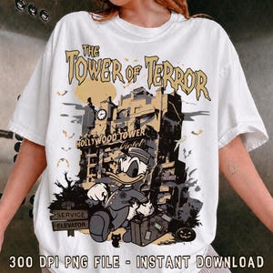 Può includere: Una t-shirt bianca con una grafica dell'Hollywood Tower Hotel e il testo The Tower of Terror. Un papero dei cartoni animati in uniforme da fattorino si trova davanti all'edificio, accompagnato da pipistrelli, una zucca e un cartello Service Elevator.