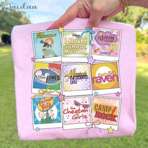 Puede incluir: Una funda de almohada rosa claro con nueve imágenes cuadradas coloridas de programas de Disney Channel, incluyendo "Kim Possible", "High School Musical" y "Lizzie McGuire". Cada imagen está enmarcada con un borde blanco y decorada con estrellas y lazos.