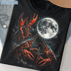 Puede incluir: Camiseta negra con un diseño gráfico de tres cangrejos rojos con grandes pinzas, sobre un cielo estrellado y una luna llena. El texto "DarleneCA60s" es visible en la esquina superior izquierda.