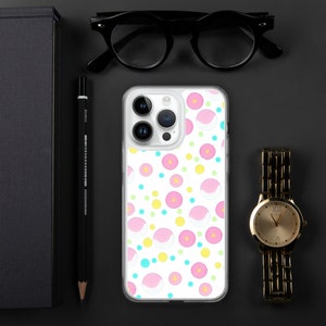 May include: A clear phone case with a white background and a repeating pattern of pink and white donuts with yellow and blue polka dots.