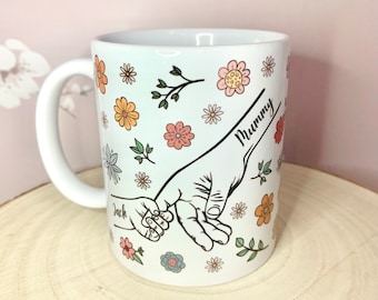 May include: White ceramic mug with a floral design and two hands holding each other. The text "Mummy" and "Jack" are written on the mug.