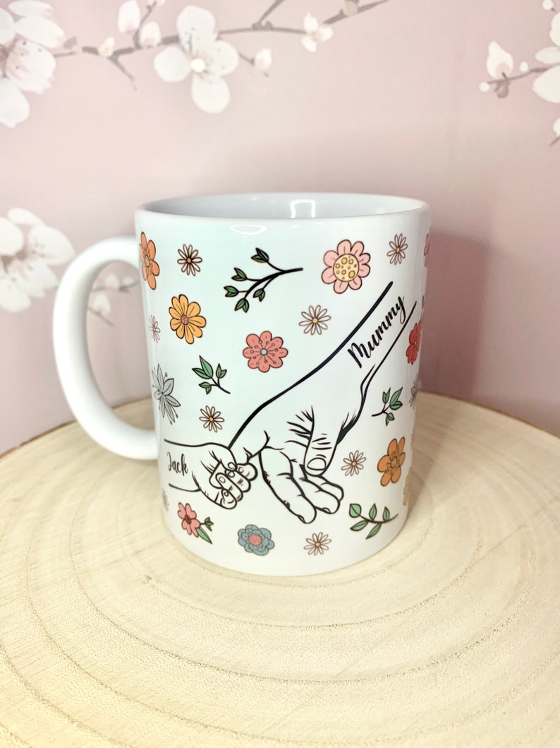 May include: White ceramic mug with a floral design and two hands holding each other. The text "Mummy" and "Jack" are written on the mug.