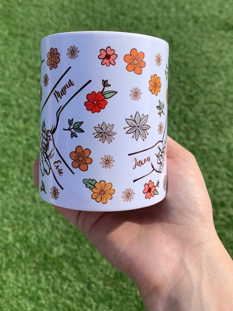 May include: White ceramic mug with a floral design and the names "Mama", "Evie", and "Jaxon" written on it.