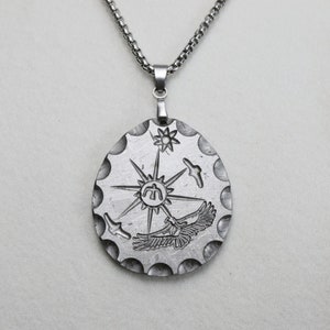 Könnte beinhalten: Eine silberne Halskette mit einem runden Anhänger, der eine stilisierte Sonne mit Strahlen, einen Vogel und ein Symbol in der Mitte zeigt. Der Anhänger ist an einer silbernen Kette befestigt.