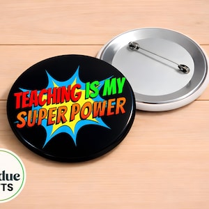 May include: Two round black pinback buttons. One button has the text "TEACHING IS MY SUPER POWER" in red, yellow, and green, with a blue burst design. The other button is silver and white. The image also includes a logo that says "iuodue GIFTS".