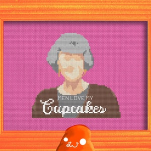 Puede incluir: Un patrón de punto de cruz en un marco rosa con un borde naranja. El patrón presenta a una mujer con cabello gris y el texto "Men love my cupcakes".
