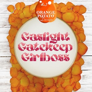 Peut inclure: Un cercle de broderie blanc avec l'inscription "Gaslight Gatekeep Girlboss" en lettres pixelisées roses. Le cercle est entouré de pétales de fleurs orange sur un fond de bois blanc. Le texte "Orange Potato Design" est écrit en blanc sur une tache orange.