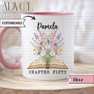 Peut inclure: Mug en céramique blanche avec une anse et un bord roses, orné d'un motif floral au-dessus d'un livre ouvert. La tasse est personnalisée avec le nom "Pamela" et le texte "CHAPTER FIFTY" avec le chiffre "50". La tasse est de 312 ml.