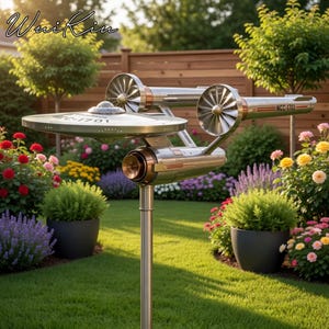 Puede incluir: Adorno de jardín metálico con forma de la U.S.S. Enterprise de Star Trek, con el texto "NCC-1701". La escultura presenta una sección de platillo circular y dos góndolas de curvatura. Montado sobre un poste metálico en un jardín florido.