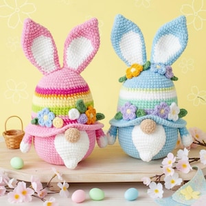 May include: Two handmade crochet Easter bunny gnomes. One is pink with a rainbow stripe and the other is blue with a striped pattern. Both have large ears, flower accents, and white beards. Easter decor.