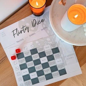 May include: A white card game with the title "Flirty Dice" printed on it. The game includes truths, dares, and shots. There are two red dice and a grid with different prompts for each number combination.