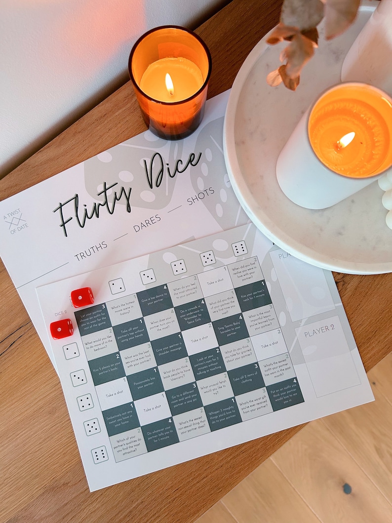 May include: A white card game with the title "Flirty Dice" printed on it. The game includes truths, dares, and shots. There are two red dice and a grid with different prompts for each number combination.