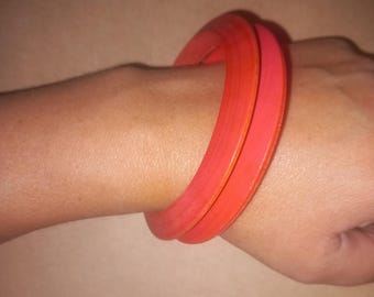 Può includere: Due braccialetti di plastica di colore arancione brillante indossati su un polso.