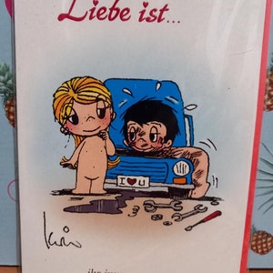 May include: A cartoon illustration of a couple. The woman is standing next to a blue car with a flat tire. The man is under the hood of the car. The text on the card reads "Liebe ist... ihr immer zu helfen." which translates to "Love is... always helping you."