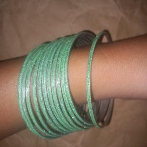 Puede incluir: Un conjunto de pulseras verdes brillantes que se llevan en la muñeca.