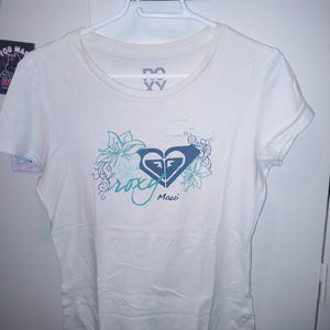 May include: White t-shirt with a blue and teal Roxy logo and floral design. The text "Maui" is printed below the logo.