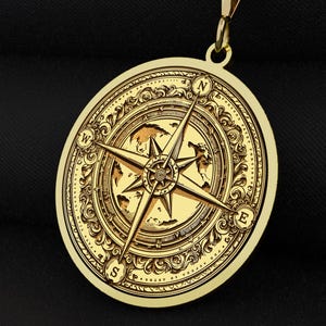May include: A gold compass pendant necklace with an intricate design. The compass features a detailed map and a compass rose with the letters N, S, E, and W.