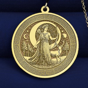 Op de afbeelding: Goudkleurige hangerketting. De ronde hanger heeft een gegraveerd ontwerp van een vrouw met pijl en boog, een hert en een halve maan. De ketting heeft een fijne ketting en een karabijnsluiting.