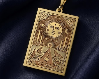May include: A gold-toned rectangular pendant necklace featuring an engraved tarot card design titled THE MOON. The engraving depicts a central moon face, two towers, two wolves, a crustacean, and stars, suspended from a delicate gold-toned chain.