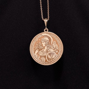 May include: A gold pendant necklace featuring a round medallion with an engraved image of Athena, the Greek goddess of wisdom and warfare. The medallion also features an owl and a spear.