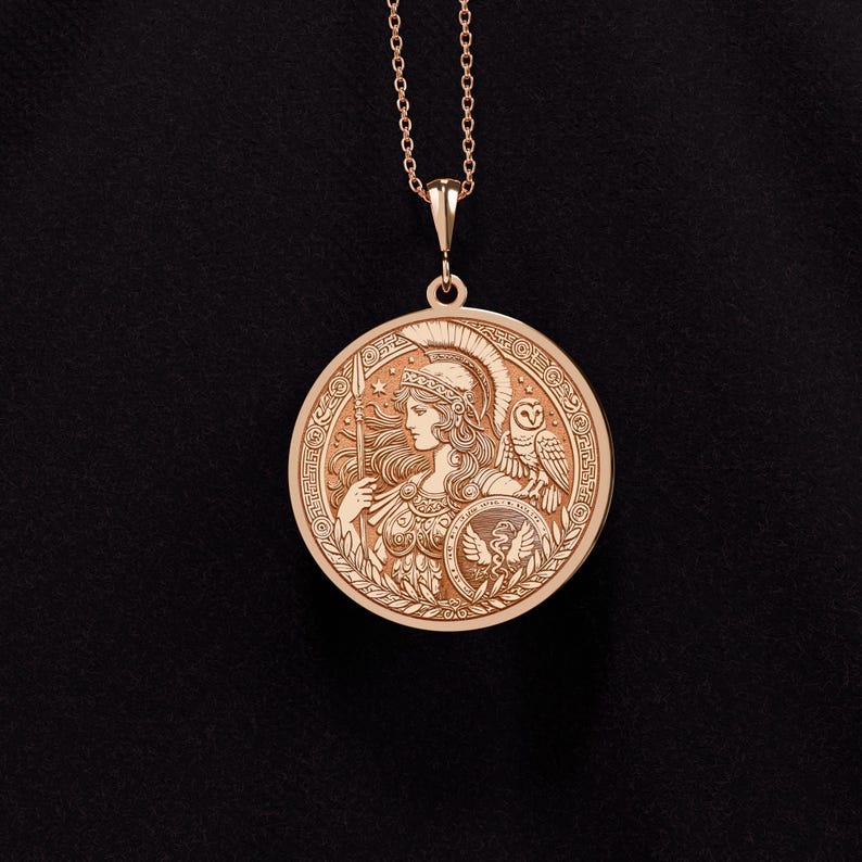 May include: A gold pendant necklace featuring a round medallion with an engraved image of Athena, the Greek goddess of wisdom and warfare. The medallion also features an owl and a spear.