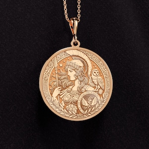 May include: A gold pendant necklace featuring a round, detailed design of the Greek goddess Athena. The pendant depicts Athena in profile, wearing a helmet and holding a spear. An owl is perched on her shoulder, and a snake is coiled around her shield. The pendant is surrounded by a decorative border.