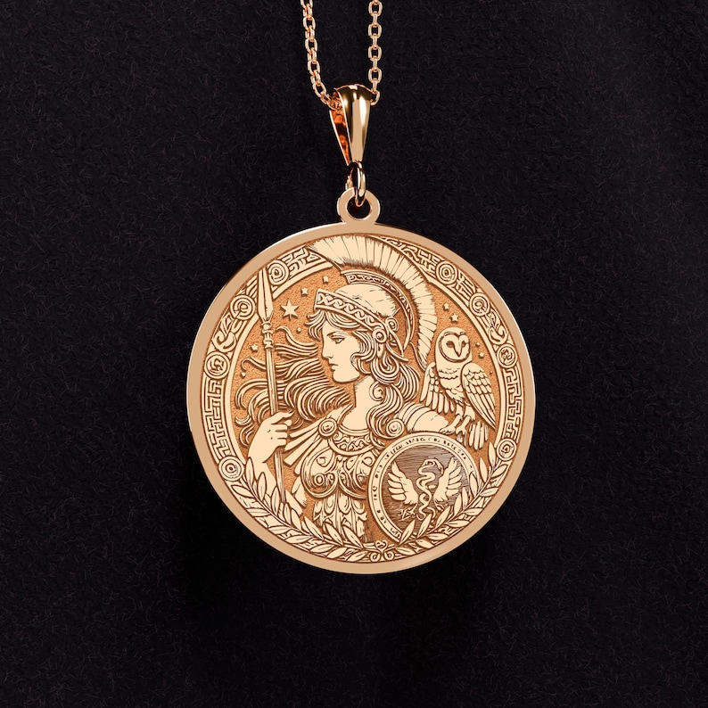 May include: A gold pendant necklace featuring a round, detailed design of the Greek goddess Athena. The pendant depicts Athena in profile, wearing a helmet and holding a spear. An owl is perched on her shoulder, and a snake is coiled around her shield. The pendant is surrounded by a decorative border.