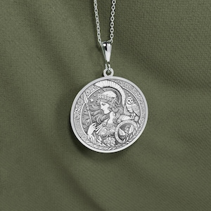 May include: Silver necklace with a round pendant featuring a detailed engraving of a woman in a helmet holding a spear, with an owl perched on her shoulder. The pendant has a Greek-inspired design.