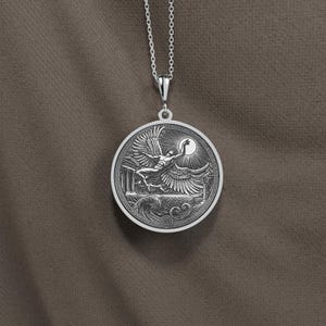 May include: A silver pendant necklace featuring a detailed relief of a winged figure reaching for the sun. The round pendant has a Greek key border and is suspended from a delicate chain. The design includes architectural elements and waves.