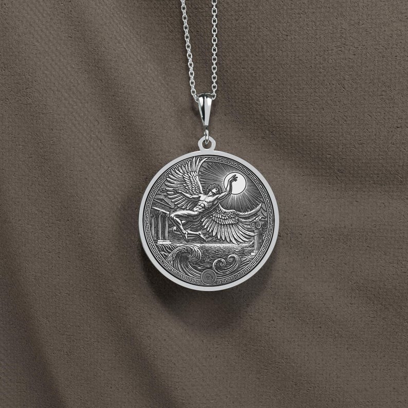 May include: A silver pendant necklace featuring a detailed relief of a winged figure reaching for the sun. The round pendant has a Greek key border and is suspended from a delicate chain. The design includes architectural elements and waves.
