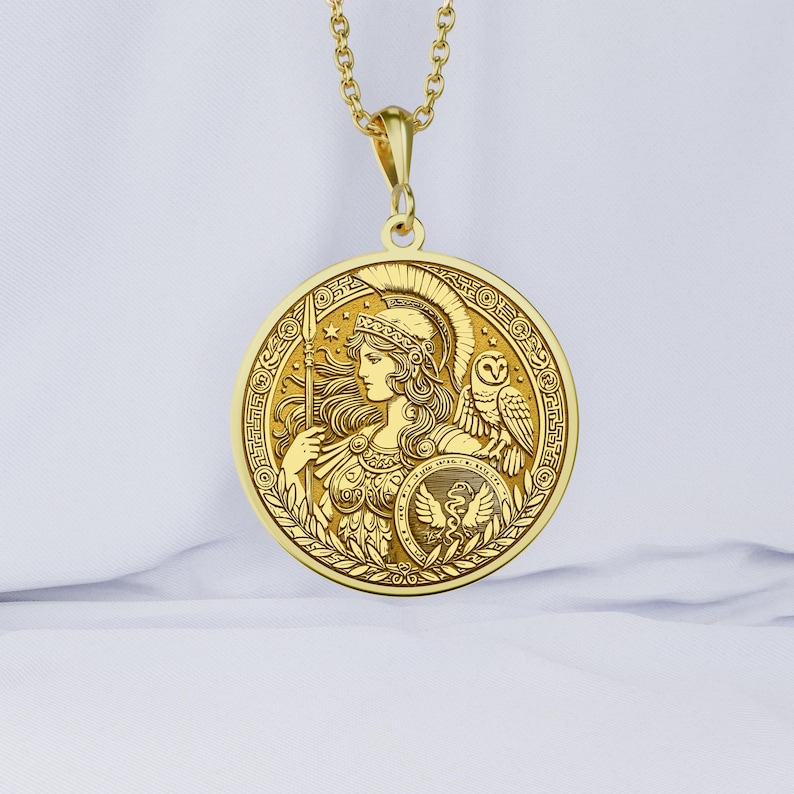 May include: A gold pendant necklace featuring a round medallion with an image of Athena, the Greek goddess of wisdom and warfare. The medallion is decorated with intricate details, including Athena's helmet, spear, and owl. The pendant is suspended from a delicate gold chain.