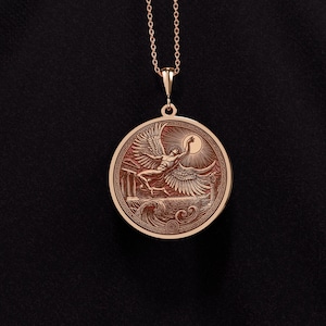 May include: A rose gold pendant necklace featuring a detailed relief of a winged figure reaching for the sun. The circular pendant has an intricate border design and is suspended from a delicate chain. The design includes architectural elements and waves.