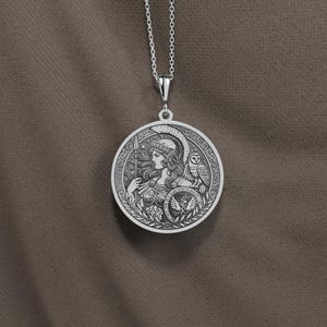 May include: Silver necklace with a round pendant featuring a detailed engraving of a woman in a helmet with an owl perched on her shoulder. The pendant has an inscription around the edge.