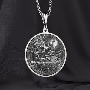 May include: A silver pendant necklace featuring a detailed relief of a winged figure reaching towards a sun, set against a backdrop of waves and classical architecture. The pendant is round with a decorative border and hangs from a silver chain.