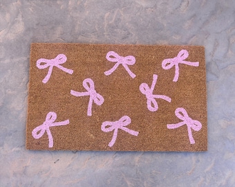 May include: A brown coir doormat with pink bow designs.