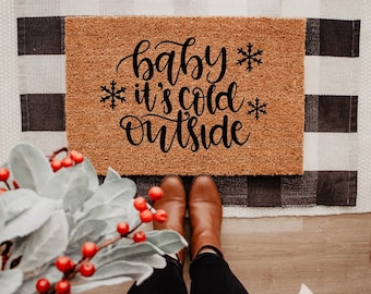 May include: A brown coir doormat with the text "baby it's cold outside" in black cursive lettering and snowflakes.