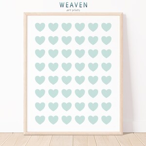Puede incluir: Una impresión artística enmarcada con un patrón de corazones verde azulado claro sobre un fondo blanco. La obra de arte está en un marco de madera clara. Las palabras "WEAVEN" y "art prints" están impresas en la parte superior de la imagen.