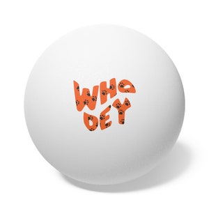 May include: White table tennis ball with the words "Who Dey" printed in orange with black paw prints.