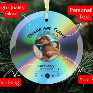 May include: A round, iridescent glass ornament with a photo of a couple in the center. The ornament has a music player design with the text "TAYLOR AND TRAVIS HOLIDAY 2023" and "Love Story Taylor Swift" on it.
