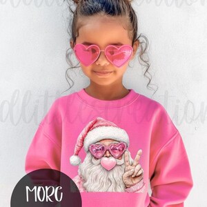 May include: A pink sweatshirt featuring a graphic of Santa Claus wearing heart-shaped sunglasses and a peace sign. The Santa graphic has a pink heart-shaped bubblegum bubble. The words "MORE OPTIONS" are in a black circle.