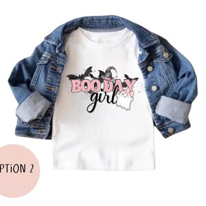 May include: White t-shirt with a pink and black graphic that says "Boo Day Girl" with a ghost and witch hat.