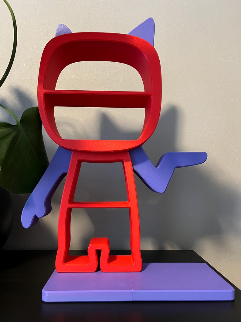 May include: A red and purple shelf unit shaped like a cartoon character. The character has a large head with two shelves, a body with one shelf, and a single arm outstretched. The character is standing on a purple base.